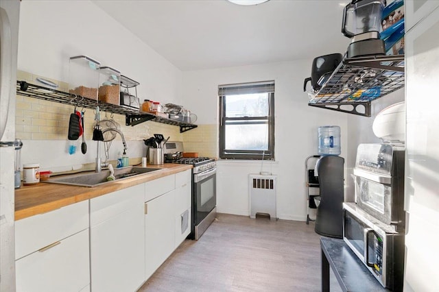 2 E Mill Dr Apt 2H, Great Neck, NY 11021 - kitchen with stainless steel range with gas stovetop, radiator heating unit, light wood-style flooring, white cabinetry, and backsplash