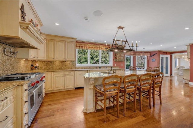 kitchen featuring pendant lighting, a kitchen breakfast bar, light stone countertops, an island with sink, and range with two ovens