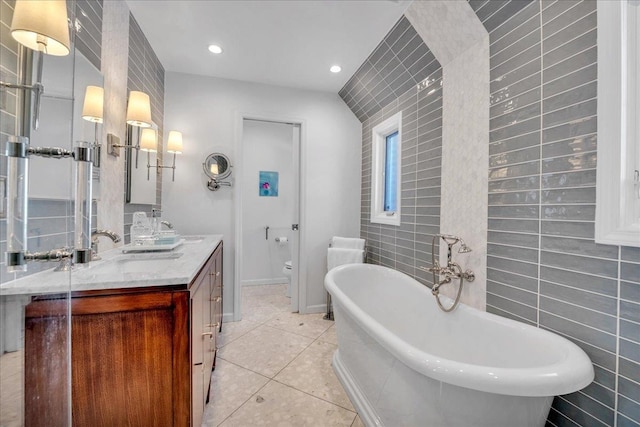 bathroom with tile walls, a tub to relax in, vanity, toilet, and tile patterned floors