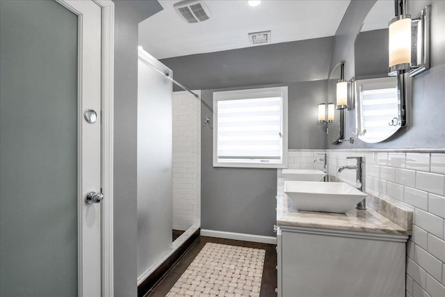 bathroom with vanity, tiled shower, and tile walls