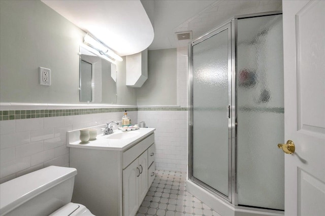 bathroom with tile walls, vanity, toilet, and an enclosed shower