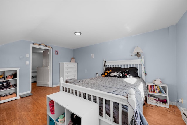 bedroom with hardwood / wood-style flooring, vaulted ceiling, and a baseboard heating unit