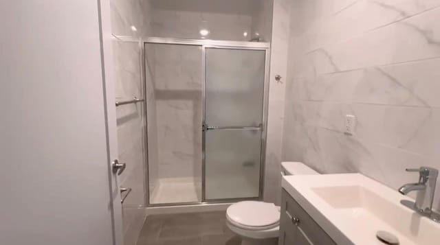 bathroom featuring vanity, a shower with shower door, and toilet