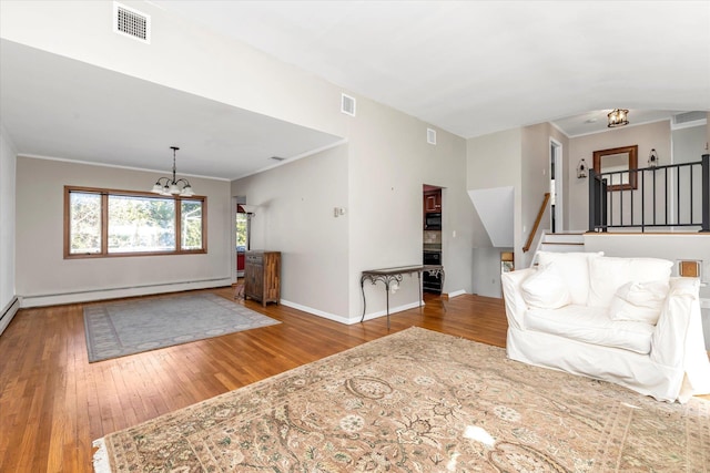 unfurnished living room featuring baseboard heating, crown molding, wood-type flooring, and a notable chandelier