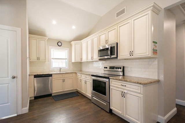 kitchen featuring appliances with stainless steel finishes, light stone counters, vaulted ceiling, dark wood-type flooring, and sink