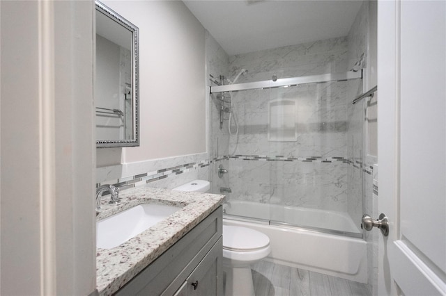 full bathroom featuring vanity, bath / shower combo with glass door, tile walls, and toilet