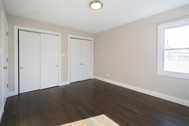 unfurnished bedroom with two closets and dark hardwood / wood-style floors