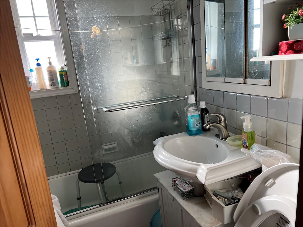 bathroom with sink, shower / bath combination with glass door, tile walls, and tasteful backsplash