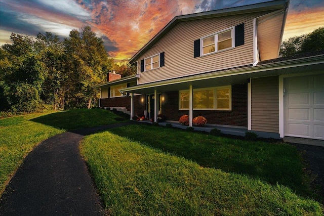 back house at dusk featuring a porch, a garage, and a yard