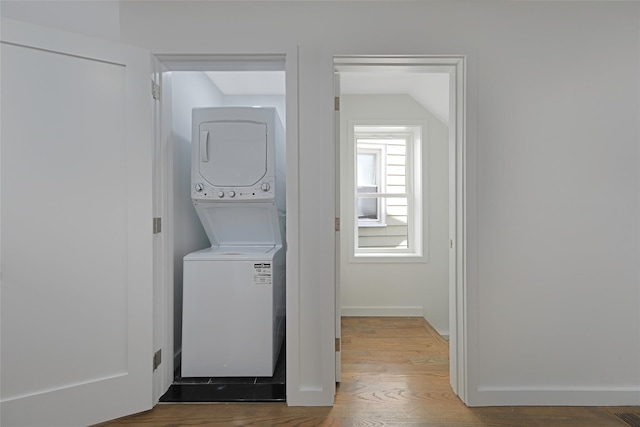 laundry area featuring wood-type flooring and stacked washer / dryer