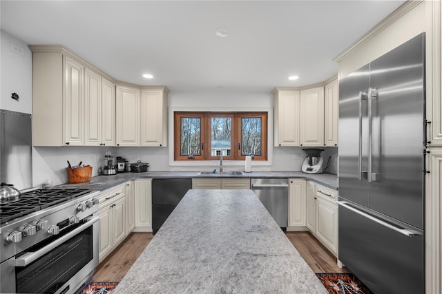 kitchen featuring high end appliances, light wood-style floors, a sink, and dark stone countertops