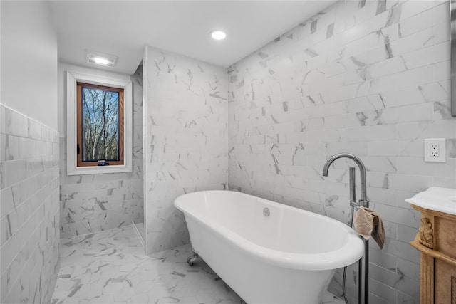 bathroom featuring marble finish floor, tile walls, recessed lighting, a soaking tub, and vanity