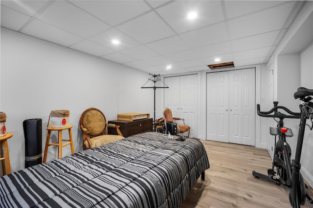 bedroom featuring multiple closets, recessed lighting, a drop ceiling, and light wood-style floors