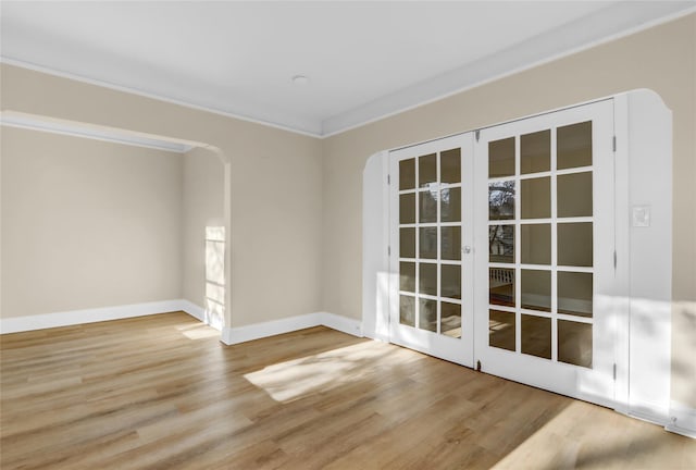 empty room featuring french doors, light wood-type flooring, and ornamental molding