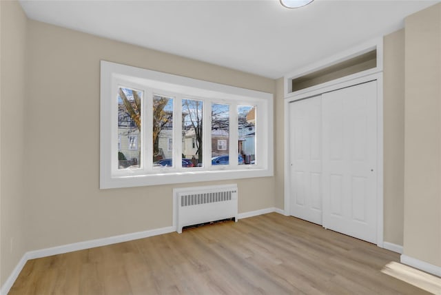 unfurnished bedroom featuring a closet, radiator, and light hardwood / wood-style floors