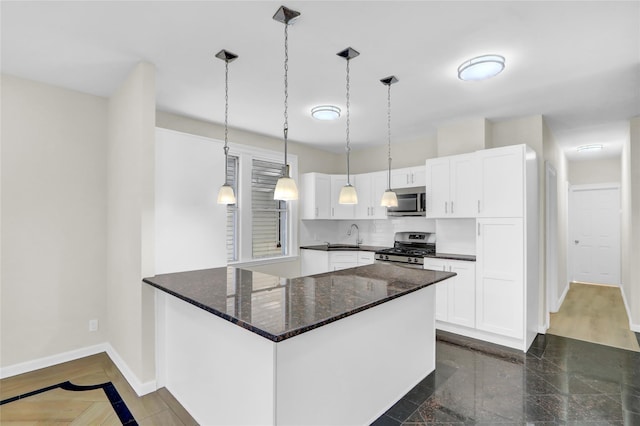 kitchen with appliances with stainless steel finishes, sink, dark stone countertops, white cabinetry, and hanging light fixtures