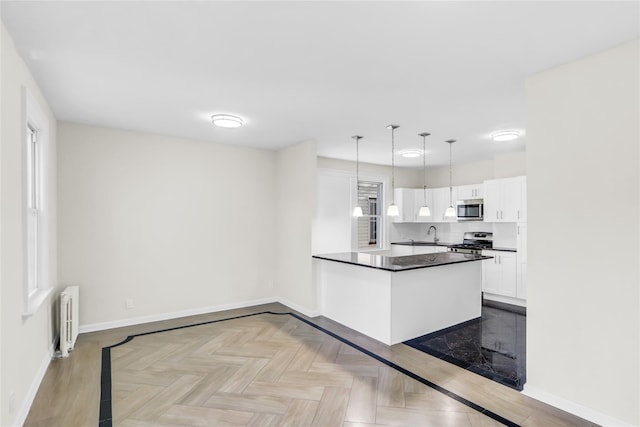 kitchen featuring white cabinetry, radiator heating unit, hanging light fixtures, light parquet floors, and appliances with stainless steel finishes