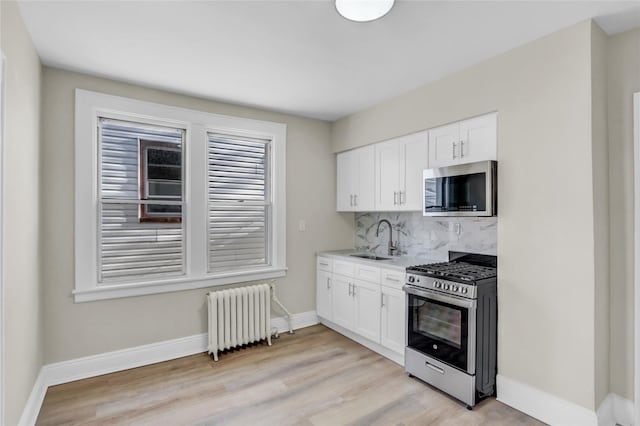 kitchen featuring radiator heating unit, sink, decorative backsplash, appliances with stainless steel finishes, and white cabinetry