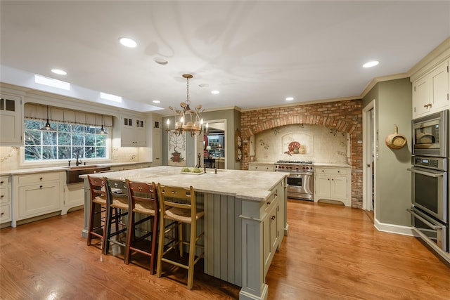 kitchen featuring decorative backsplash, hanging light fixtures, light stone countertops, a kitchen island with sink, and appliances with stainless steel finishes