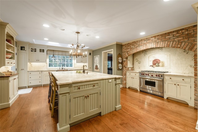 kitchen featuring light stone countertops, high end range, decorative light fixtures, a center island with sink, and decorative backsplash