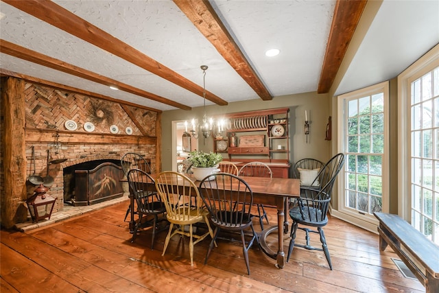 dining room with a fireplace, beam ceiling, a chandelier, and hardwood / wood-style floors