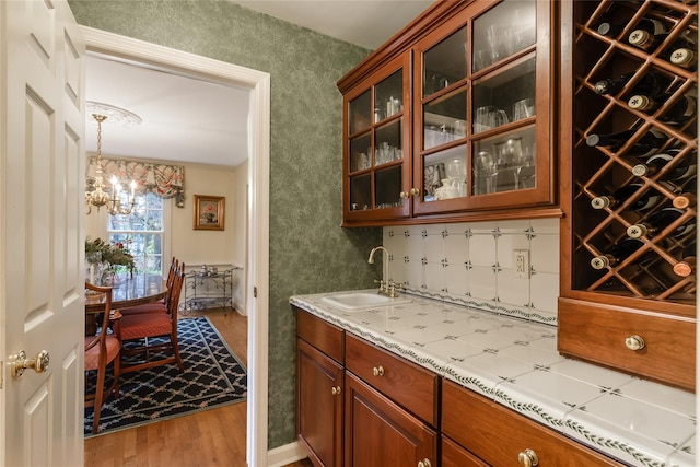 bar with sink, decorative light fixtures, an inviting chandelier, hardwood / wood-style floors, and ornamental molding