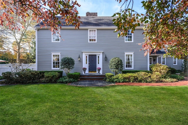 colonial-style house with a chimney, a front lawn, and fence