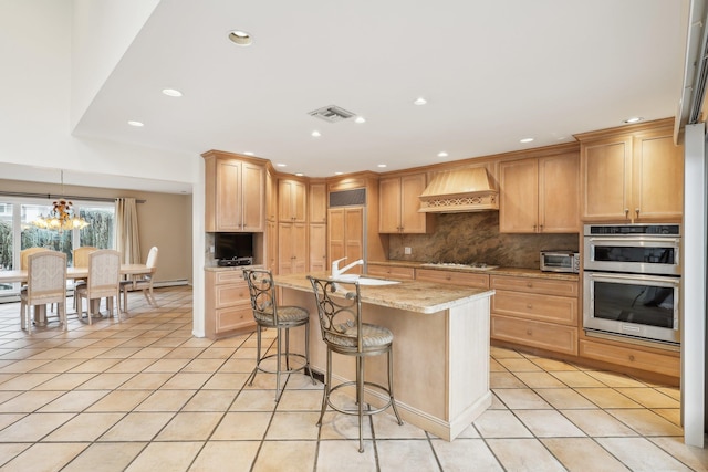 kitchen with light stone countertops, custom range hood, light tile patterned floors, and a kitchen island with sink