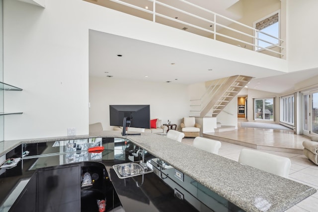 kitchen featuring sink, light tile patterned floors, stone countertops, and a high ceiling