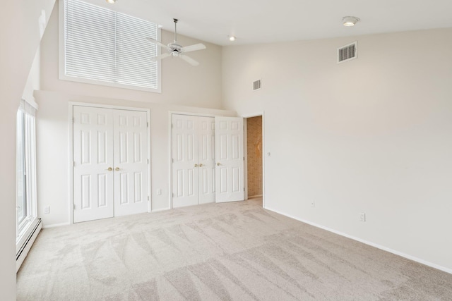 unfurnished bedroom with light carpet, two closets, ceiling fan, a baseboard heating unit, and high vaulted ceiling