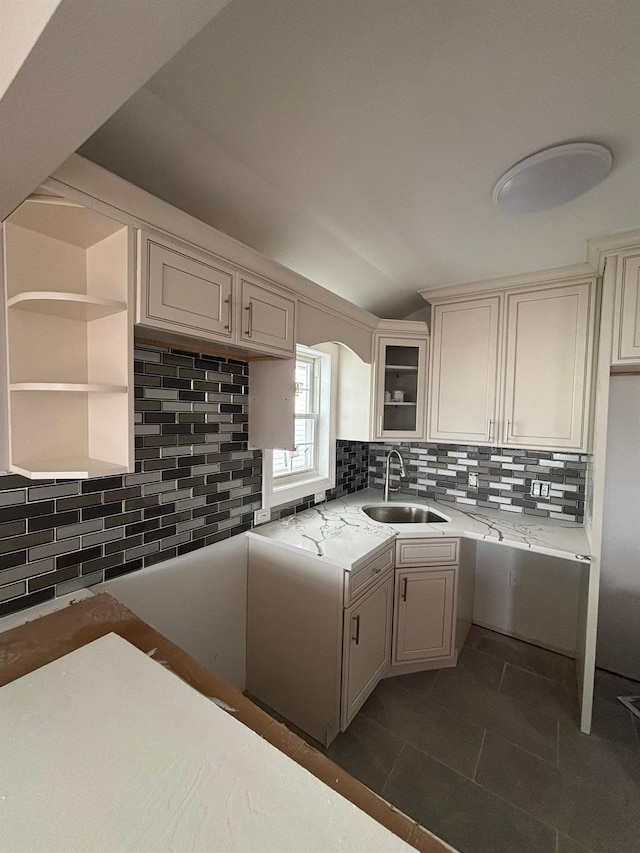 kitchen featuring backsplash, light stone countertops, sink, and dark tile patterned flooring