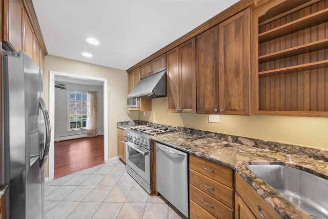 kitchen with sink, baseboard heating, dark stone counters, light tile patterned floors, and appliances with stainless steel finishes