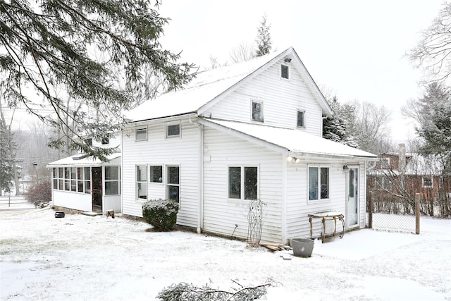 snow covered rear of property featuring a sunroom