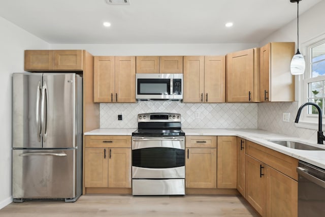 kitchen featuring pendant lighting, sink, decorative backsplash, light wood-type flooring, and appliances with stainless steel finishes