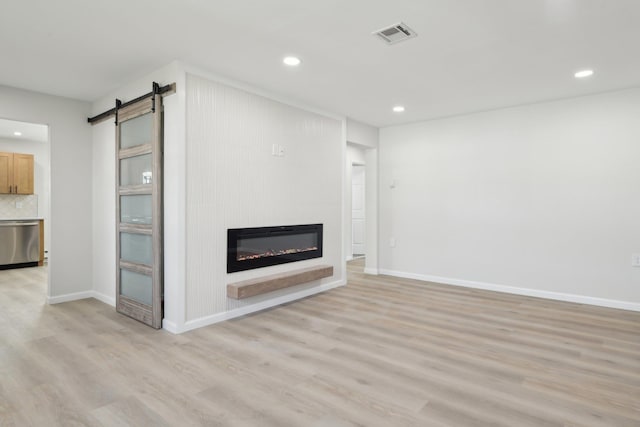 unfurnished living room featuring a fireplace, a barn door, and light hardwood / wood-style flooring