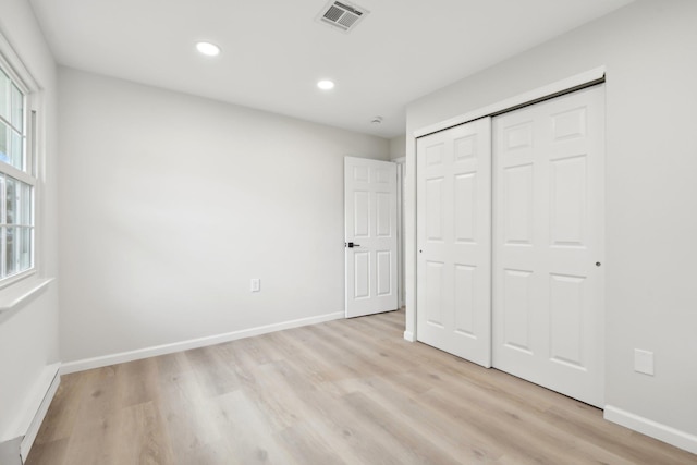 unfurnished bedroom featuring light hardwood / wood-style floors, baseboard heating, and a closet