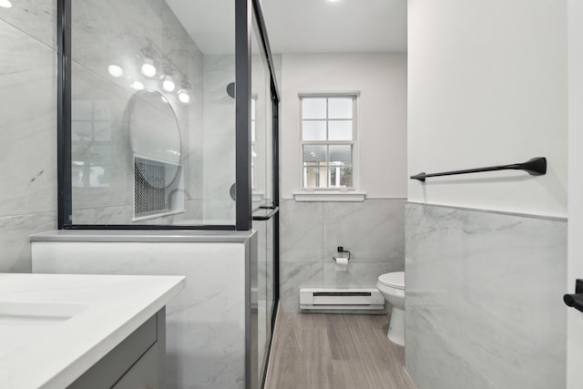 bathroom featuring walk in shower, a baseboard heating unit, toilet, vanity, and tile walls