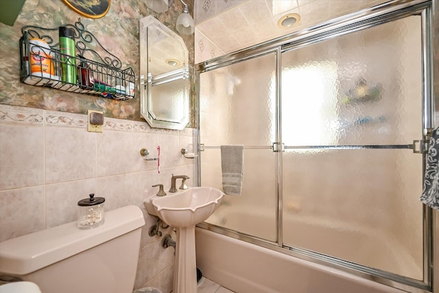 bathroom featuring bath / shower combo with glass door, tile walls, and toilet