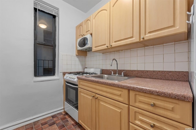 kitchen with backsplash, light brown cabinets, gas range oven, and sink