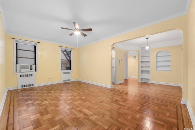 empty room featuring cooling unit, ceiling fan, built in features, parquet flooring, and radiator heating unit