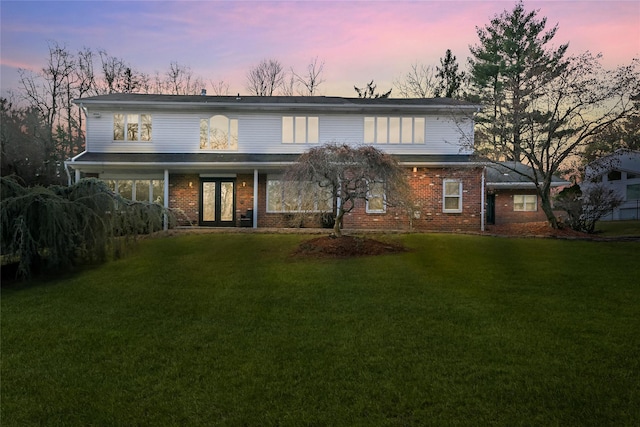 back house at dusk featuring a lawn and french doors