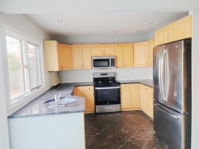 kitchen featuring appliances with stainless steel finishes, dark stone counters, light brown cabinetry, and sink