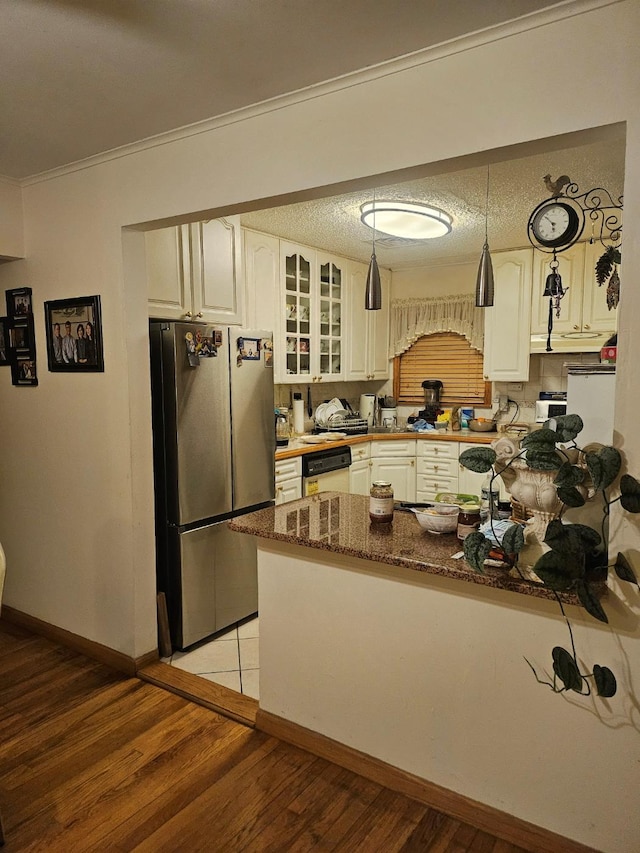 kitchen with light hardwood / wood-style flooring, stainless steel fridge, dark stone counters, white cabinets, and ornamental molding