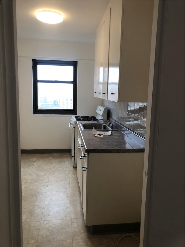 kitchen with baseboards, light tile patterned flooring, white gas stove, white cabinets, and tasteful backsplash