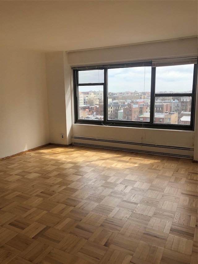 empty room featuring a baseboard radiator, plenty of natural light, baseboards, and a city view