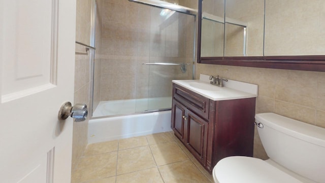 full bathroom featuring toilet, vanity, tile walls, tile patterned flooring, and combined bath / shower with glass door