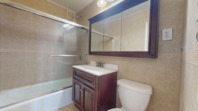 full bathroom with tile walls, enclosed tub / shower combo, vanity, and toilet