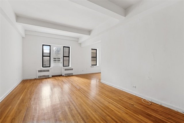 empty room with beamed ceiling, light hardwood / wood-style floors, and radiator