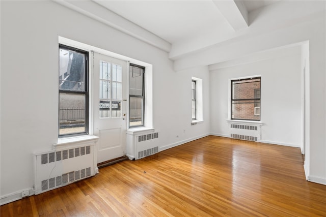 unfurnished room with radiator heating unit, plenty of natural light, and hardwood / wood-style floors