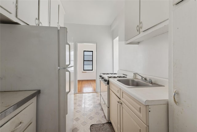 kitchen with gas stove, white cabinets, sink, and white fridge